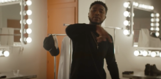 Screen Shot of Cozz in dressing room with vanity mirrors and clothes rock with clothing backdrop for "Bout It" video